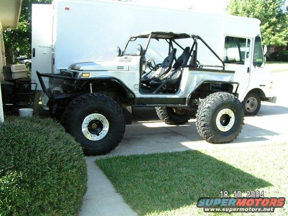 Off-road vehicle with large tires and roll cage parked next to a white box truck