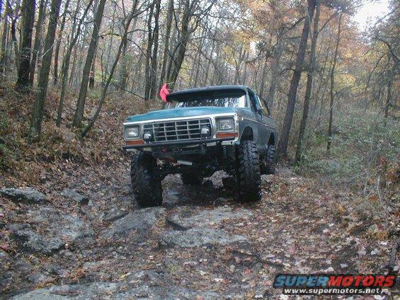 Green 1978 Ford Bronco off-roading on a leaf-covered rocky path in a forest