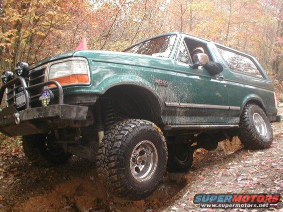 Green Ford Bronco with off-road tires on a dirt trail, front passenger side wheel elevated