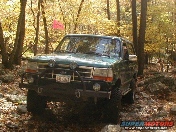 Green Ford Bronco navigating a rocky, wooded trail in the fall