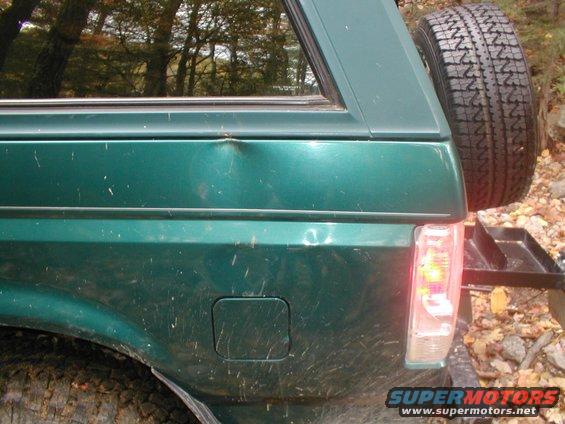 Green SUV rear quarter panel with dent, spare tire, and taillight