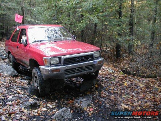 Red Toyota 4Runner with a pink flag on the roof rack, navigating a rocky forest trail