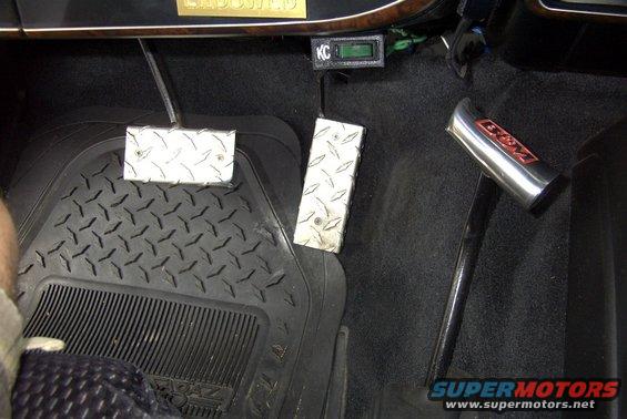 Interior view of a vehicle showing diamond plate brake and gas pedals, a KC gauge, and a B&M shifter