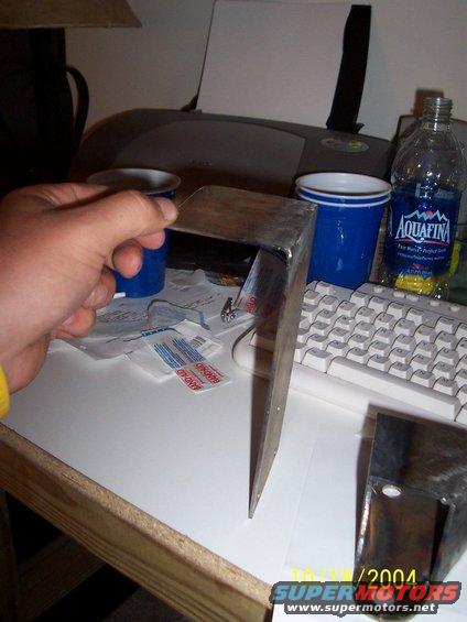 Metal bracket held by a hand, with a keyboard and water bottle in the background