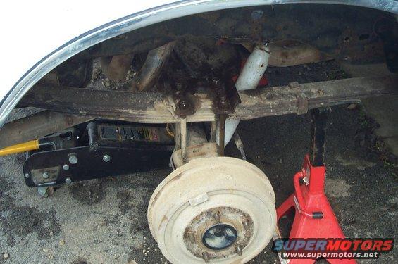 Vehicle's rear axle, leaf springs, and shock absorber are visible, supported by a jack and jack stand