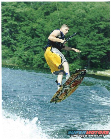 Wakeboarder mid-air over water with trees in background