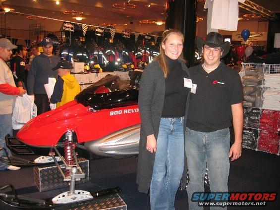 People stand next to a red snowmobile with '800 REVO' on its side