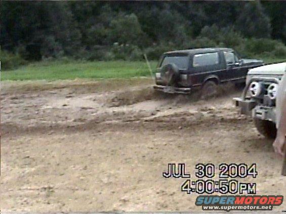 Two off-road vehicles driving through mud. One is a dark SUV with a spare tire on the back