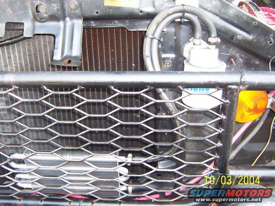Close-up of vehicle's front grille with honeycomb pattern, showing radiator and some engine components. Date stamp reads 10/03/2004