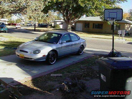 Silver sedan parked in a driveway next to a trash can and basketball hoop