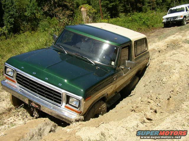 Green and tan 1978 Ford Bronco stuck in mud on a dirt track