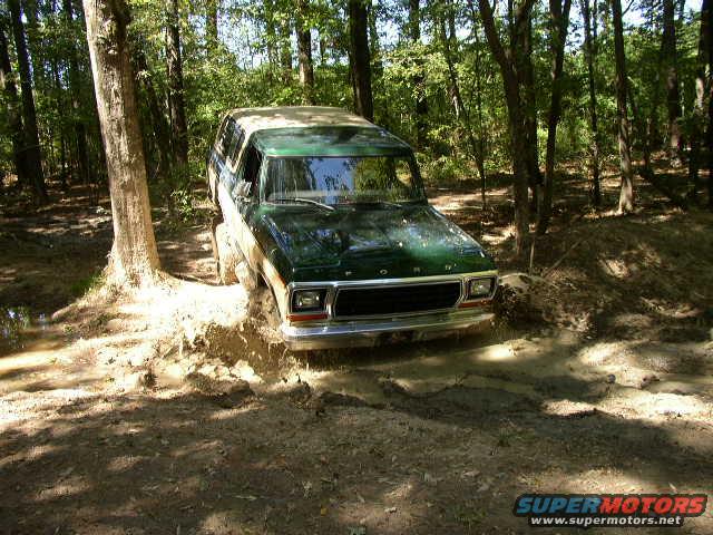 Green 1978 Ford Bronco driving through mud, front grille visible
