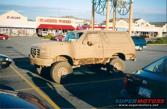 Mud-covered SUV parked in a lot, with Rogers Video and Cash stores in background. License plate visible