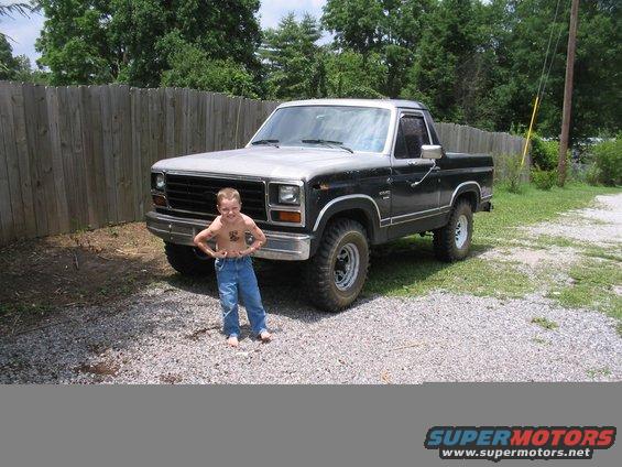 Boy flexing in front of a black and silver pickup truck. The truck appears to be from the early 1980s