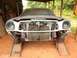 1977 Ford Mustang II - The front of a car is shown with the grille and headlights removed, resting on ramps inside a covered structure.