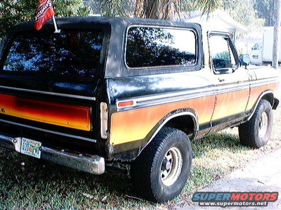 1978 Ford Bronco with orange and yellow stripe, black top, and a flag on the roof