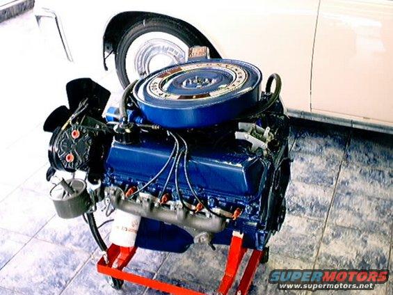 Blue engine on red stand with white car fender and wheel in background