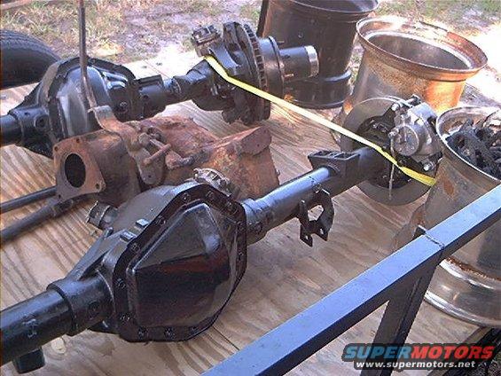 Two black vehicle axles with brake components and differential covers on a wooden surface