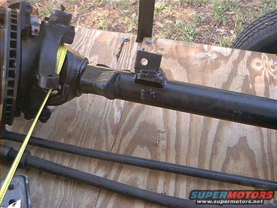 Front axle assembly with disc brake rotor and yellow measuring tape. Supermotors.net logo visible