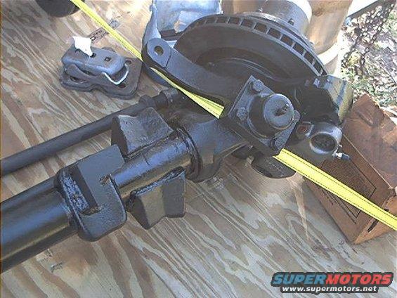 Vehicle axle and brake assembly with a yellow strap across it. Some parts are on a wooden surface