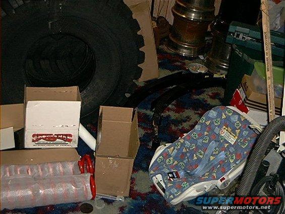 Baby car seat with a blue, patterned cover sits next to a large tire and cardboard boxes