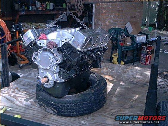 Engine block with chrome valve covers and intake manifold, suspended by chains over a tire