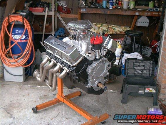 V8 engine on an orange stand in a garage, with an air compressor and tools nearby