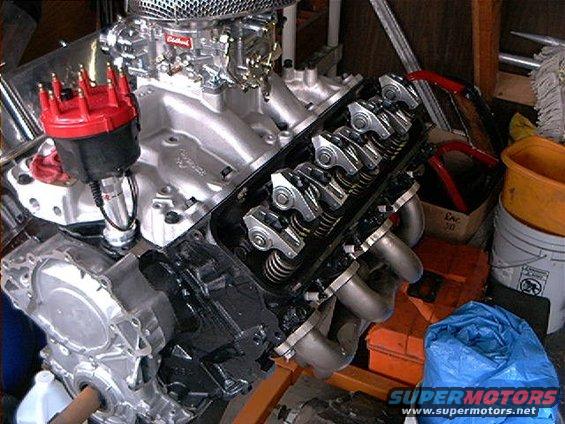 Engine block with valve covers removed, showing rocker arms and springs. Chrome air cleaner and red distributor cap visible
