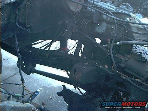 Undercarriage of a vehicle with exposed frame, suspension, and wiring. Some parts appear rusted or damaged