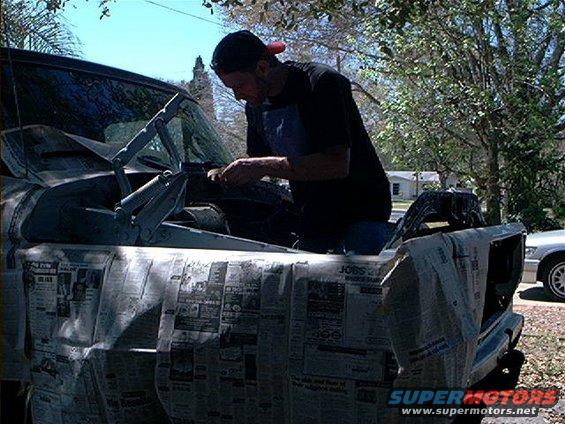1978 Ford Bronco with hood open, covered in newspaper, being worked on by a man