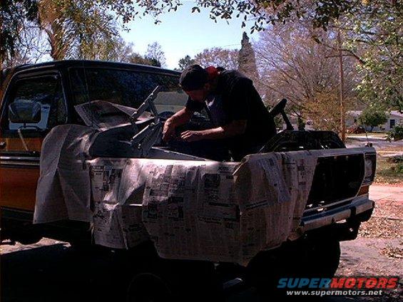 1979 Ford Bronco front end covered in newspaper, man working on engine