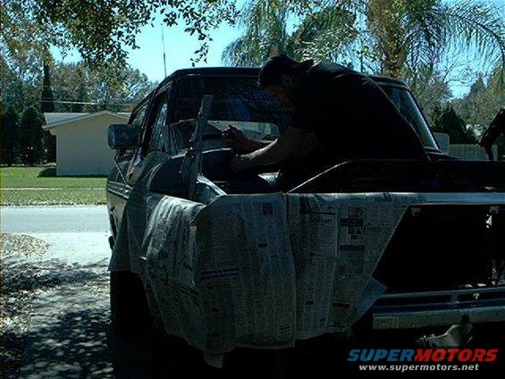 Man working on the engine of a 1979 Ford Bronco, front grille covered in newspaper