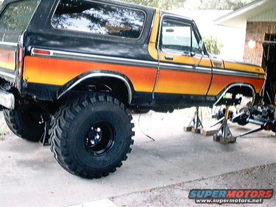 Orange and yellow striped Ford Bronco on jack stands, lifted with large tires