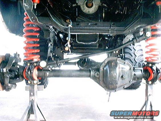 Underside of a vehicle on jack stands, showing the front axle, differential, and red coil springs
