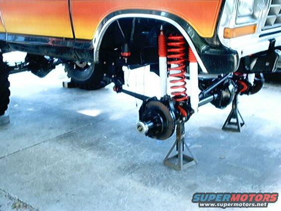 Orange and yellow Ford Bronco front suspension on jack stands, showing red shocks and springs