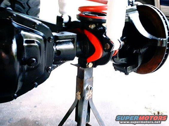 Rear axle assembly with red coil spring and white shock absorber, supported by jack stands
