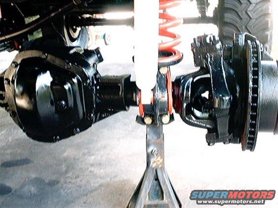 Close-up of a vehicle's rear axle and suspension components, including a shock absorber and coil spring, supported by a jack stand