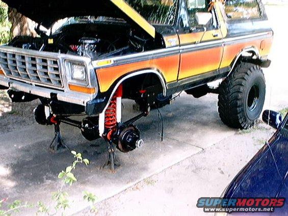 Ford Bronco on jack stands with hood up and front suspension removed. Orange and yellow stripe detail on side