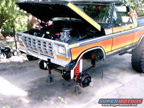Black and orange Ford Bronco with hood open, front end raised on jack stands, showing suspension