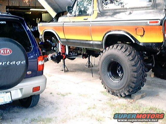 Orange and yellow Ford Bronco on jack stands, front axle removed, next to a blue Kia Sportage