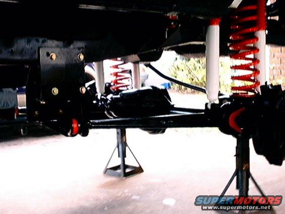 Close-up of vehicle suspension with red coil springs and white shocks, supported by jack stands
