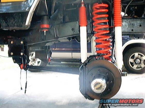 Underside of a vehicle showing red coil springs, white shock absorbers, and a brake rotor