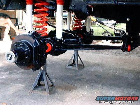 Close-up of a vehicle's front suspension with red springs and white shocks on jack stands. Disc brake assembly visible