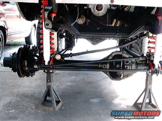 Undercarriage of a vehicle on jack stands, showing suspension and drivetrain components
