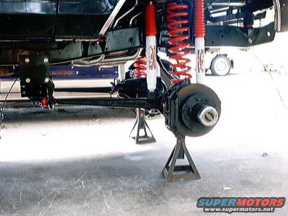 Vehicle frame and suspension components, including red coil springs and white shock absorbers, are supported by jack stands