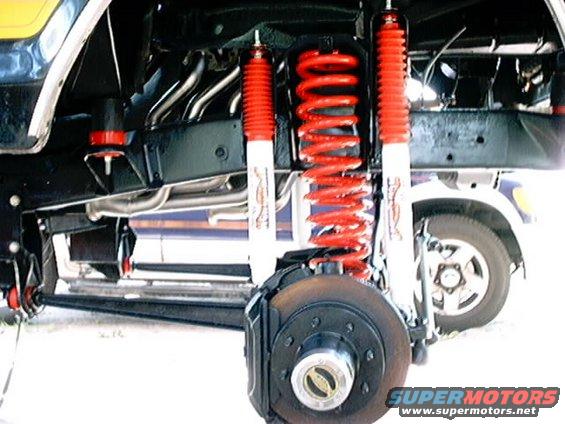 Close-up of red coilover shocks and suspension parts, with a vehicle wheel visible in the background