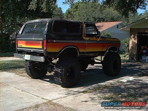 Lifted 1978 Ford Bronco with orange, yellow, and red stripe paint on the side, parked on a driveway