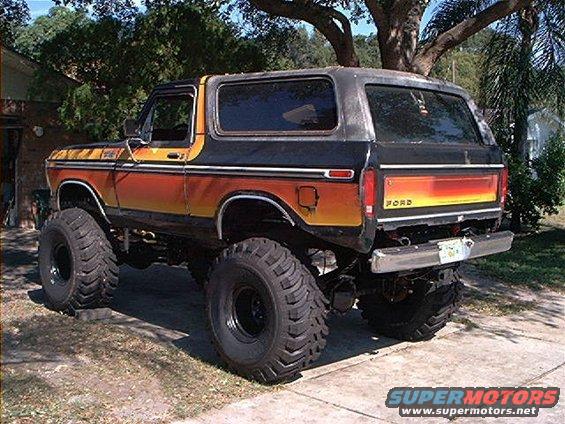 Lifted 1978 Ford Bronco with orange and black gradient paint and large off-road tires, viewed from the rear