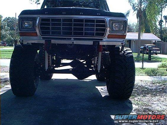 1979 Ford Bronco lifted with large tires, front view. Silver grille, orange turn signals, black hood