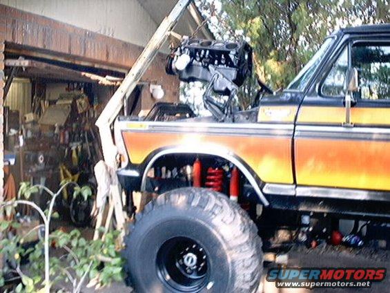1979 Ford Bronco with hood up, engine being lowered in. Lifted suspension and big tires visible
